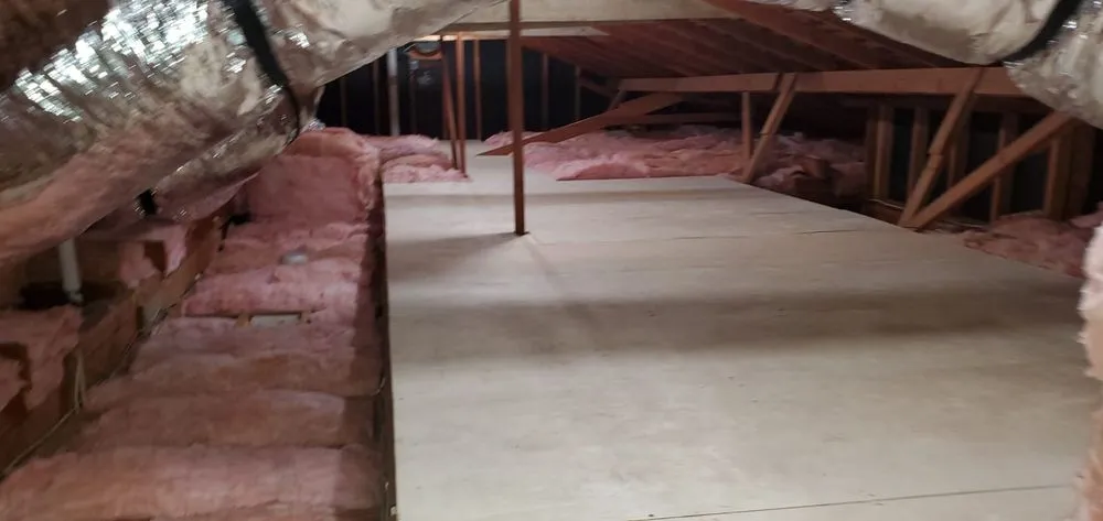 An attic space in SanJose with installed insulation by InsulationGuruInc.dbaHVACGuru, showcasing pink fiberglass insulation and ductwork.